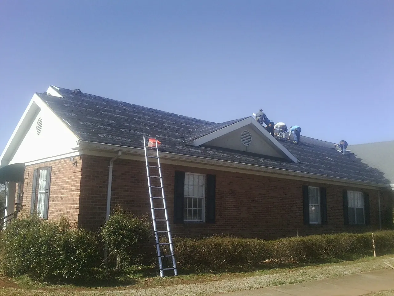 Crew tearing shingles off a brick ranch roof with a ladder set — Metal Roof Repair work by our crew in Hope