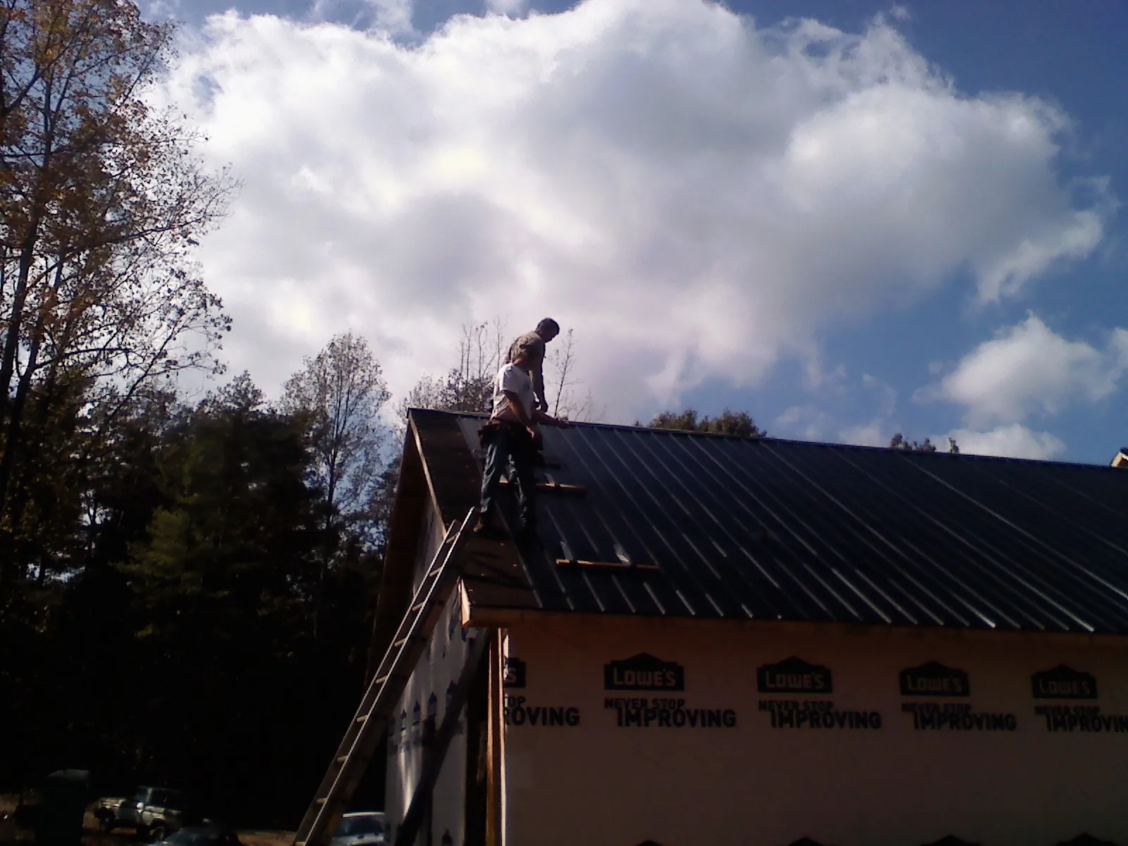 Roofer fastening dark metal panels high against a cloudy sky, from a Roof Inspection job in Hope